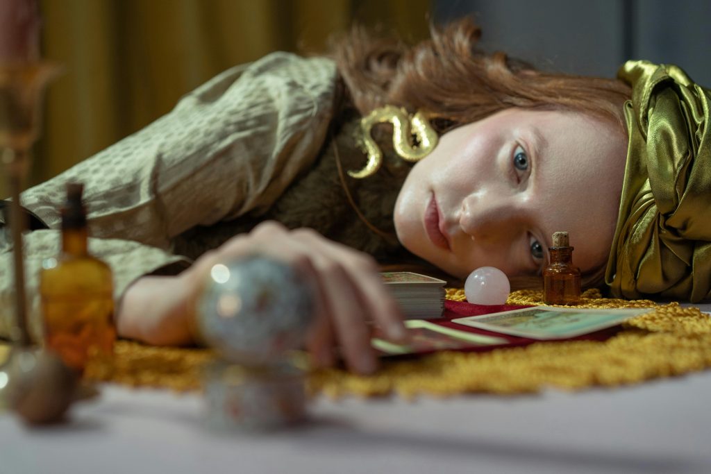 Enigmatic woman lying with tarot cards and crystal ball in a mystical setting.