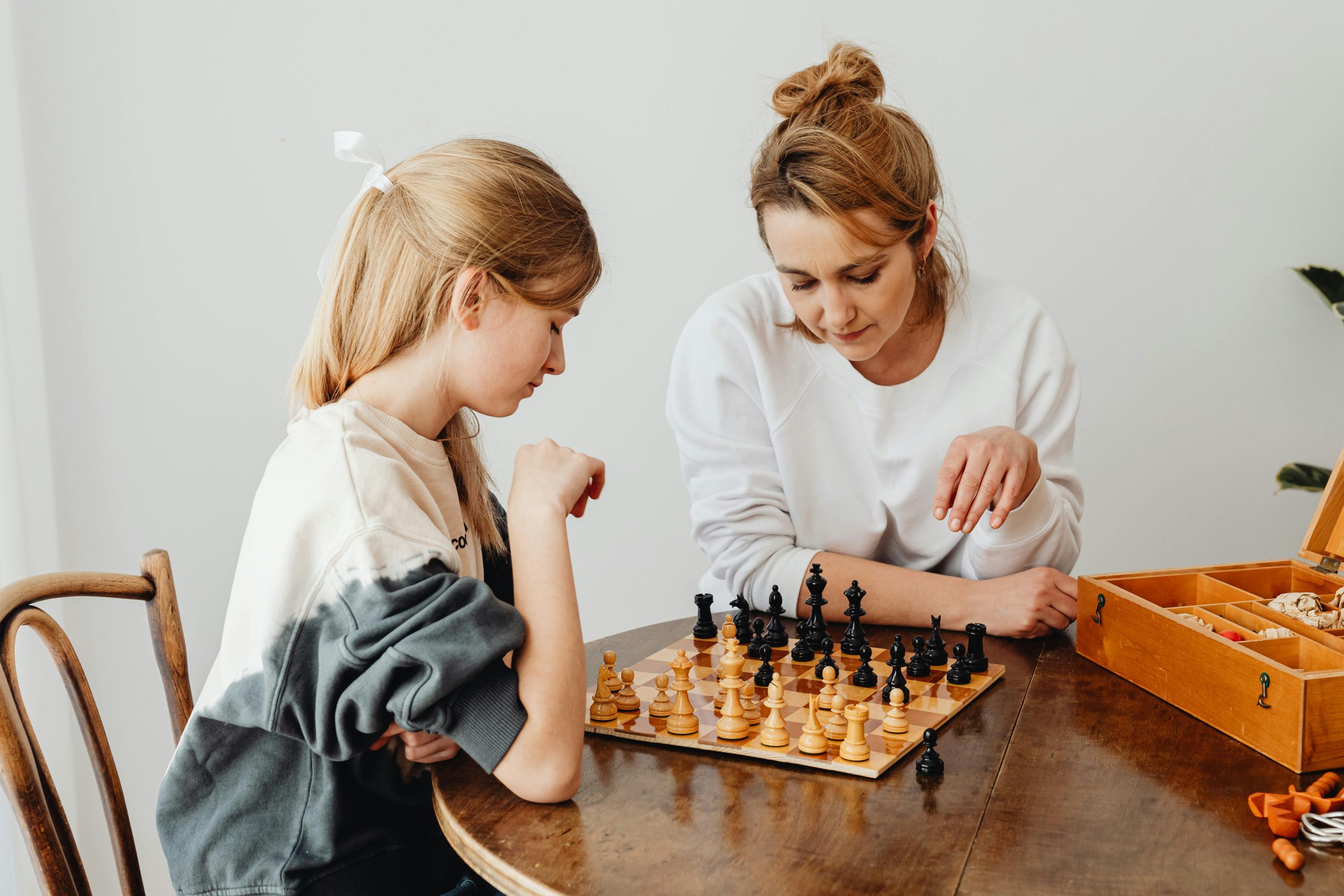 A mother and daughter engaging in a thoughtful chess game indoors, showcasing family bonding.